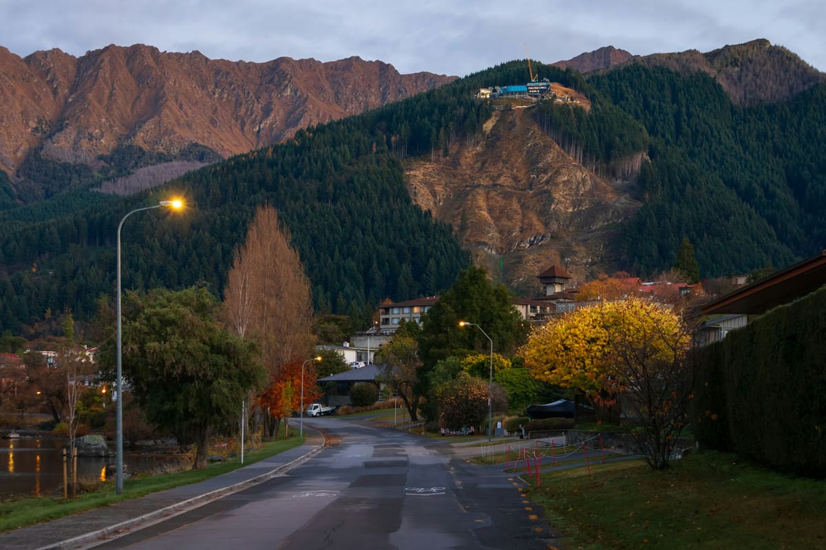 A quiet road at dusk below a forested mountain